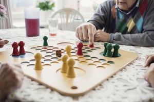 Äldre person spelar sällskapsspel vid ett bord i ett ljust rum