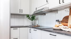 Modernt kök i lägenhet med vita skåp, mörk bänkskiva och spishäll