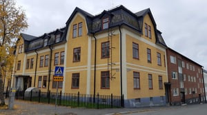 Flerfamiljshus i gul puts med mörkt tak och röda fönsterkarmar