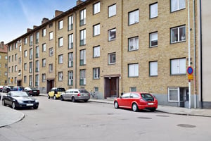 Flerfamiljshus med fasad av gul tegel, parkerade bilar längs gatan och en cykel vid entrén