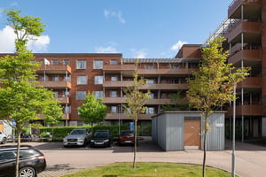 Bostadshus i tegel med flera våningar med balkonger, parkering och grönområde under en molnig himmel