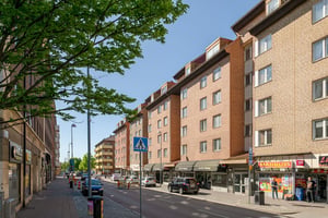 Flerfamiljshus med tegelfasad med lokaler i bottenplan, omgiven av gator under klar himmel