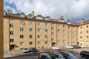 Flerbostadshus i gul tegelfasad med vindskupor, med parkering på innergården