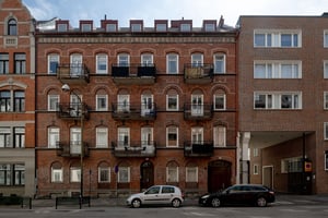 Flerbostadshus i rött tegel och grå puts med detaljer kring fönster vinskupor, längs gata med parkerade bilar