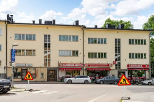 Bostadshus med flera butiker och restauranger i bottenvåningen, med parkerade bilar och vägarbetsskyltar framför