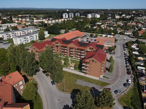 Flygvy över bostadshus i ett bostadsområde med röda tak, parkering och grönska