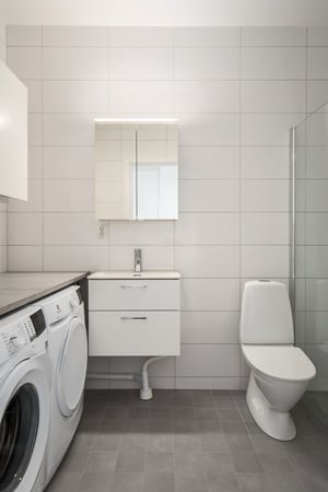 Modernt badrum med tvättmaskin, torktumlare, kommod med spegelskåp och toalett