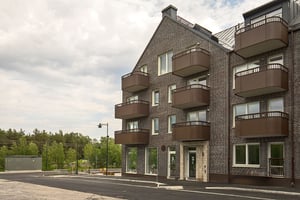 Flerfamiljshus i tegel med balkonger och entré, omgivet av grönska
