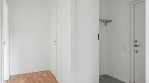 Inflyttningsklart rum med vita väggar, parkettgolv och en dörr till ett klädförråd