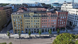 Flerfärgad fasad på en rad moderna byggnader längs en gata, med träd och parkeringsplatser i förgrunden
