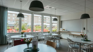 Tomt rum i modern gemensamhetslokal med runda bord, stolar och stora fönster
