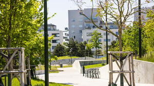 Grönskande bostadsgård med gångväg, bänkar och flerfamiljshus i bakgrunden