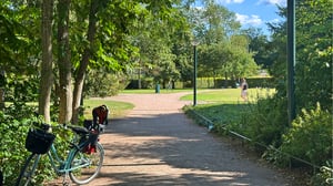 Parkmiljö, i Lund, med grusgång, träd och grönskande växtlighet, med en parkerad cykel i förgrunden
