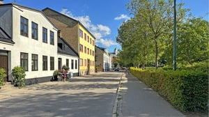 Gatuhus i Lund med gångbana, träd och grönska under klar himmel