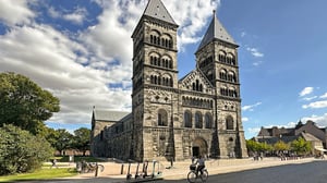 Lunds domkyrka med två torn i sten, omgiven av träd och blå himmel