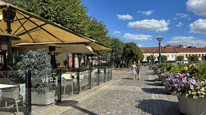 Två personer promenerar på en solig gata i Lund med uteservering och blomsterurnor
