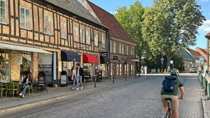 Kullerstenbelagd gata i Lund med historiska hus, caféer och personer som promenerar och sitter utomhus i stadsmiljö