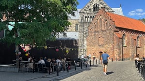 Uteservering i Lund vid historisk tegelkyrka med besökare på kullerstensgata och människor som sitter utomhus