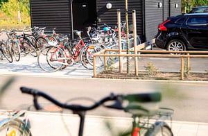 Cykelparkering vid ett svart flerbostadshus med flera parkerade cyklar och en bil