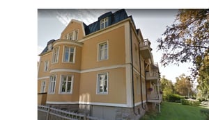 Gult flerfamiljshus med vita fönster och balkonger i grönskande omgivning