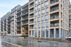 Modernt flerfamiljshus med fasad av tegel, stora fönster och balkonger, beläget vid en våt asfalterad gata