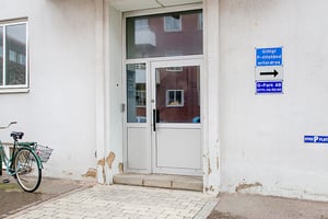 Vit entrédörr med glaspartier på en byggnad, cykel med korg parkerad till vänster, och skyltar som indikerar parkeringsregler på väggen