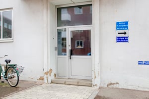 Ingång med glasdörrar bredvid en blå skylt med information om parkering, en cykel står lutad mot väggen till vänster