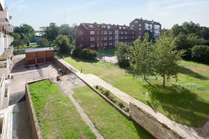 Bostadsområde med flerfamiljshus i rött tegel, omgivna av gröna gräsmattor och träd. En gångväg och parkeringsplats syns i förgrunden