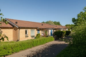 Flerbostadshus i tegel, i radshuslänga med grön häck mot gata