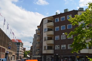 Flerfamiljshus i tegel med balkonger, beläget vid en gata med parkeringsskyltar och byggnader under en blå himmel