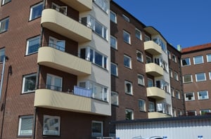 Flerfamiljshus med balkonger och fasad av tegel och ljusa detaljer, under en klarblå himmel