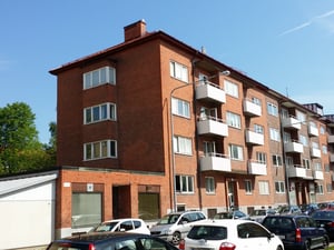Flerbostadshus i tegel med balkonger och parkerade bilar framför, soligt väder