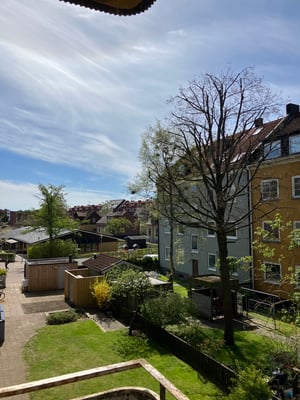 Bostadsområde med lägenhetshus, träd, gårdsbyggnader och grönska under en klar himmel