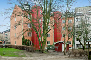 Flerbostadshus med färgglada fasader, träd och en liten röd byggnad i förgrunden