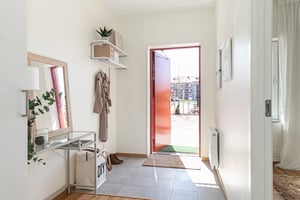 Ljus och välkomnande hall med en öppen dörr som vetter ut mot en innergård, inredd med hatthylla, spegel och planta