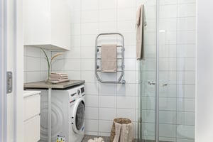 Badrum med vitkaklade väggar, tvättmaskin, handdukshängare, duschkabin och dekorativa handdukar