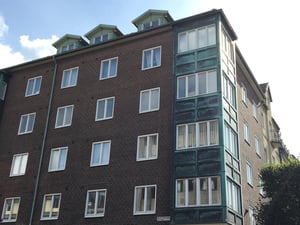 Flerbostadshus i tegel med gröna detaljer och stora fönster, under en klar himmel
