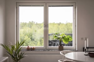 Inflyttningsklart vardagsrum med stort fönster, växter och utsikt mot grönska