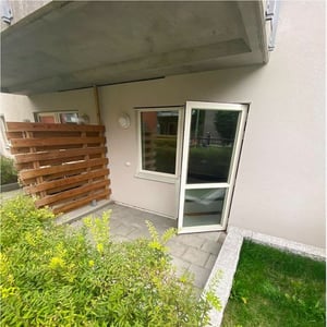 Uteplats under balkong, stenlagt golv och gröna buskar