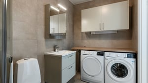 Tvättstuga med tvättmaskin, torktumlare, handfat och förvaringsskåp i modern inredning