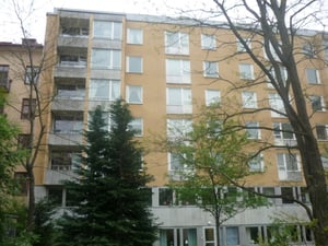 Gul flerbostadshus med fem våningar, omgiven av träd och grönska