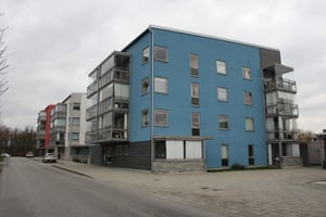 Flerfamiljshus med blå fasad och balkonger, beläget vid en asfalterad gata