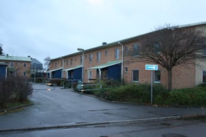 Radhusområde med tegelbyggnader, parkeringsplats och växtlighet under en mulen himmel. En pilskylt syns vid infarten