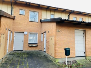 Tegelradhus med två våningar, vita dörrar och fönster. En stenlagd entré med en grön brevlåda vid sidan