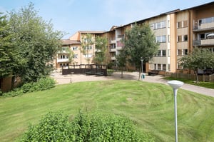 Flerfamiljshus med fasader i ljus tegel, omgivna av grönområden och träd, med en öppen innergård