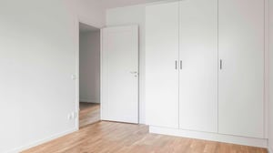 Minimalistiskt sovrum med vita garderober, en öppen dörr och parkettgolv i trä