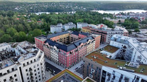 Flygfoto över ett bostadsområde med flerfamiljshus, gröna tak och omgivande grönska nära en sjö