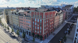 Flerfärgat bostadskvarter med moderna fasader, omgivande träd och en bred gata under en klar himmel