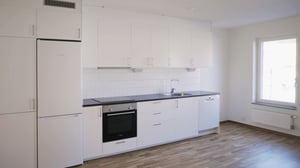 Vit och modern köksinteriör med glaskeramikhäll, inbyggd ugn, diskho och kylskåp samt vita skåpluckor och ljus trägolv