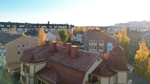 Utsikt över bostadskvarter med flerbostadshus, höstfärgade träd och en äldre byggnad med rött plåttak